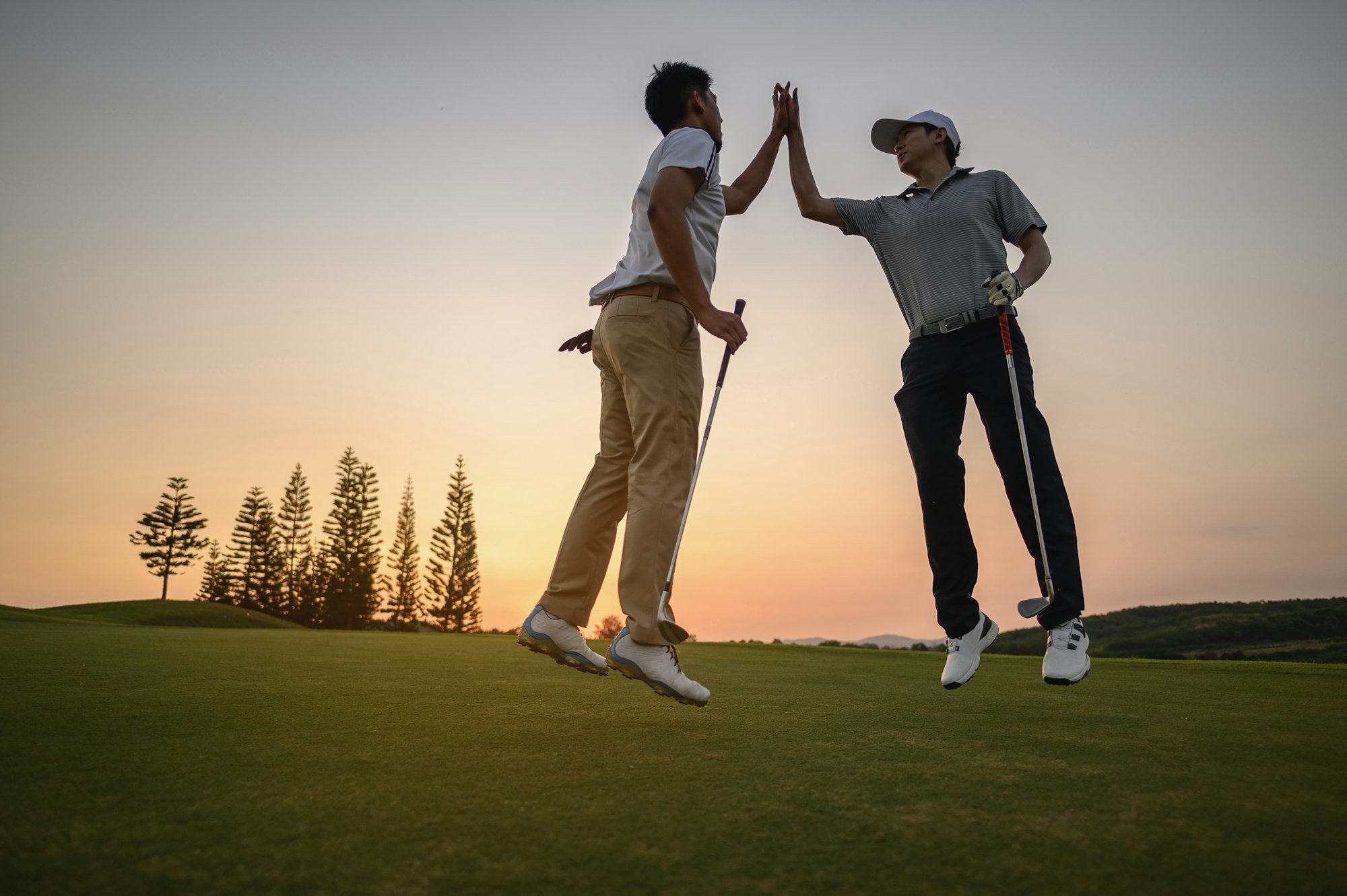 2 golfers tag their hands when golf is accomplished at the green grass golf course at sunset.